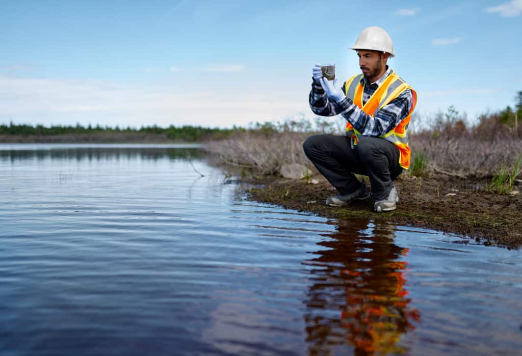 Portait of a professional scientist with protective gear examining the marsh lands in Canada and taking sample of marine plant life for research